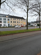 Der Lichtmast vor dem beigen Gebäude über dem Fahrradweg