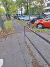 Das Farbbild zeigt einen Ausschnitt des Parkstreifens in der Mitte der Straße "Stadtwaldgürtel"; mitabgebildet mittig zwei an einmal einer Parkplatzbegrenzung,einmal an einem Verkehrschildträger fixierte Schrottfahrräder. Aufenthaltsdauer beider jeweils länger als zwei Jahre. 