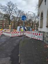 Foto einer Baustellenabsperrung, durch die ein ca. ein Meter breiter Weg führt, der aber als getrennter Geh- und Radweg ausgeschildert ist.