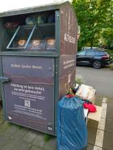Voller Altkleidercontainer und diverser Unrat in Kartons daneben