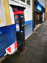 Rot-weiße Baustellenbeschilderung liegt seit Wochen hinter einem Parkscheinautomat