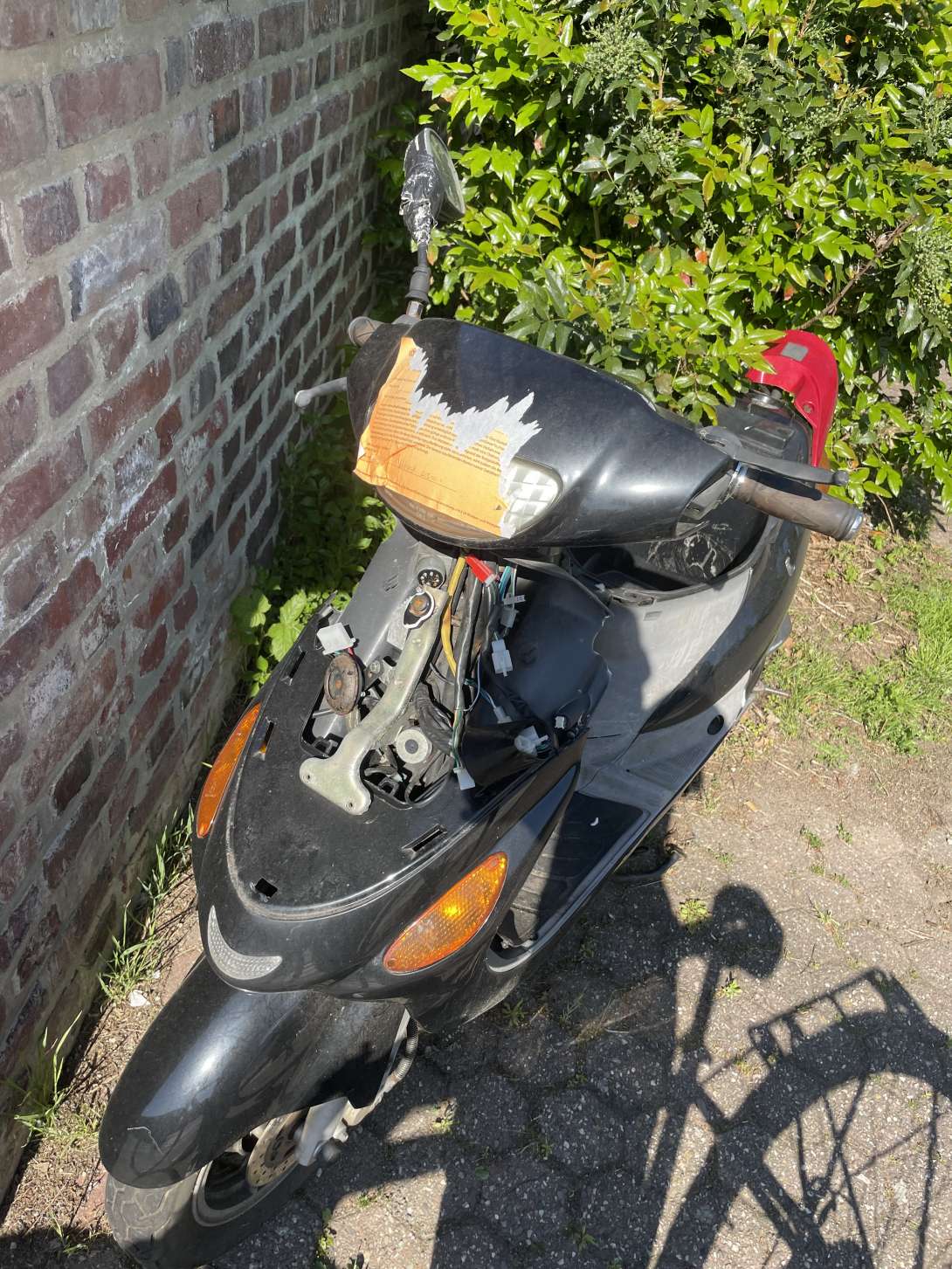 Moped mit einem offenen Motor. Auf dem Lenker klebt ein abgerissenes orangenes Schild